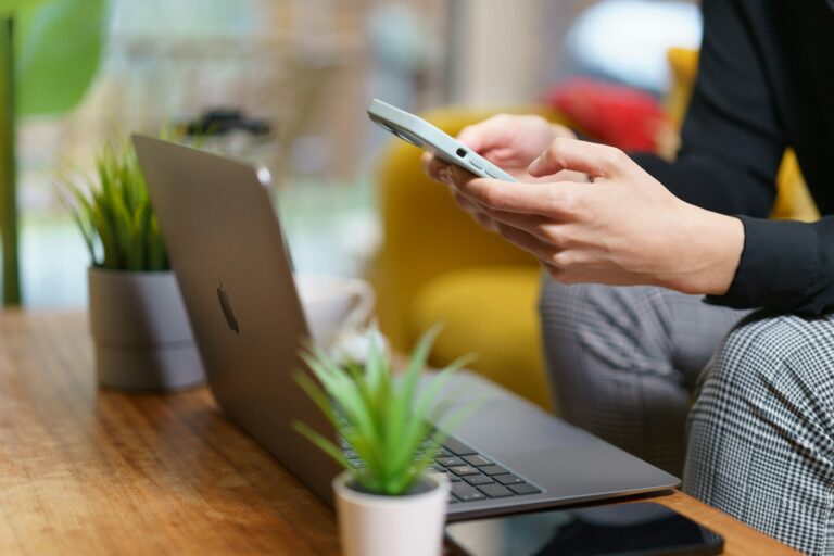Osoba używająca telefonu komórkowego siedząc przed laptopem